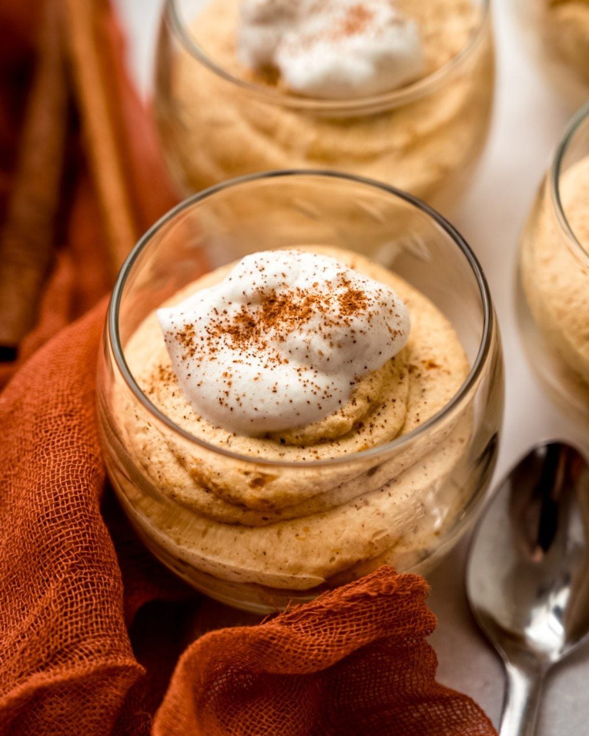 Light and airy pumpkin mousse piped into a clear glass dish, finished with a dollop of whipped cream and a delicate dusting of ground cinnamon