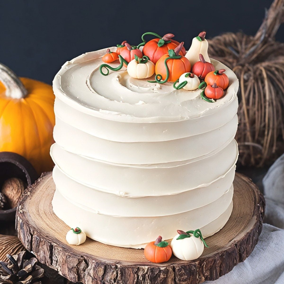 Smooth beige-frosted pumpkin spice latte Thanksgiving cake decorated with tiny handcrafted fondant pumpkins and gourds on a wooden cake board.