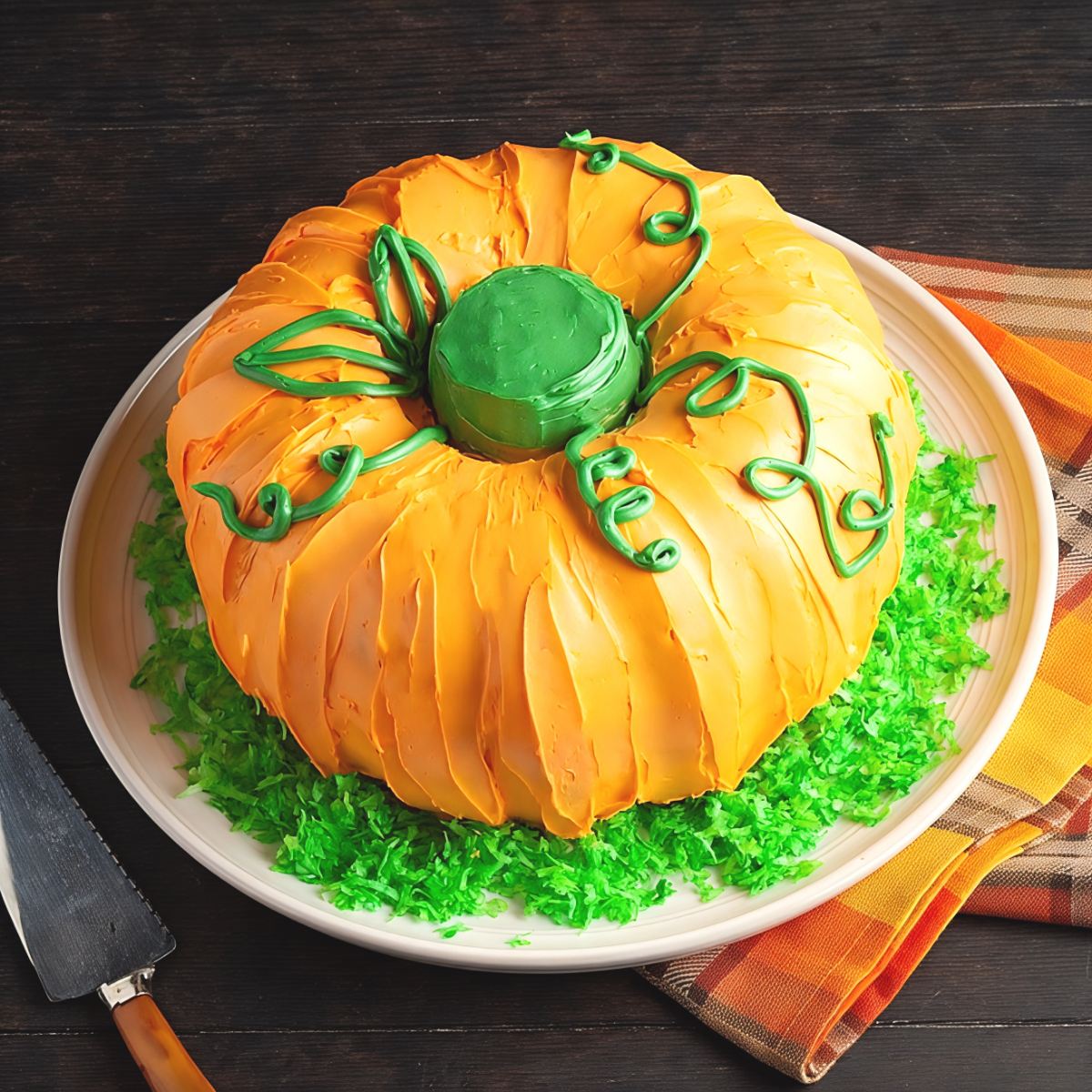 Festive pumpkin-shaped Thanksgiving bundt cake frosted in bright orange icing with green piped vines and stem.