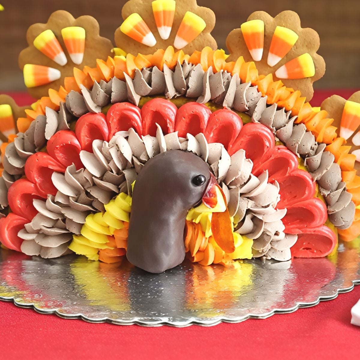 Creative sideways turkey Thanksgiving cake featuring detailed buttercream feathered piping, candy-corn-topped cookies, and a chocolate-covered head.