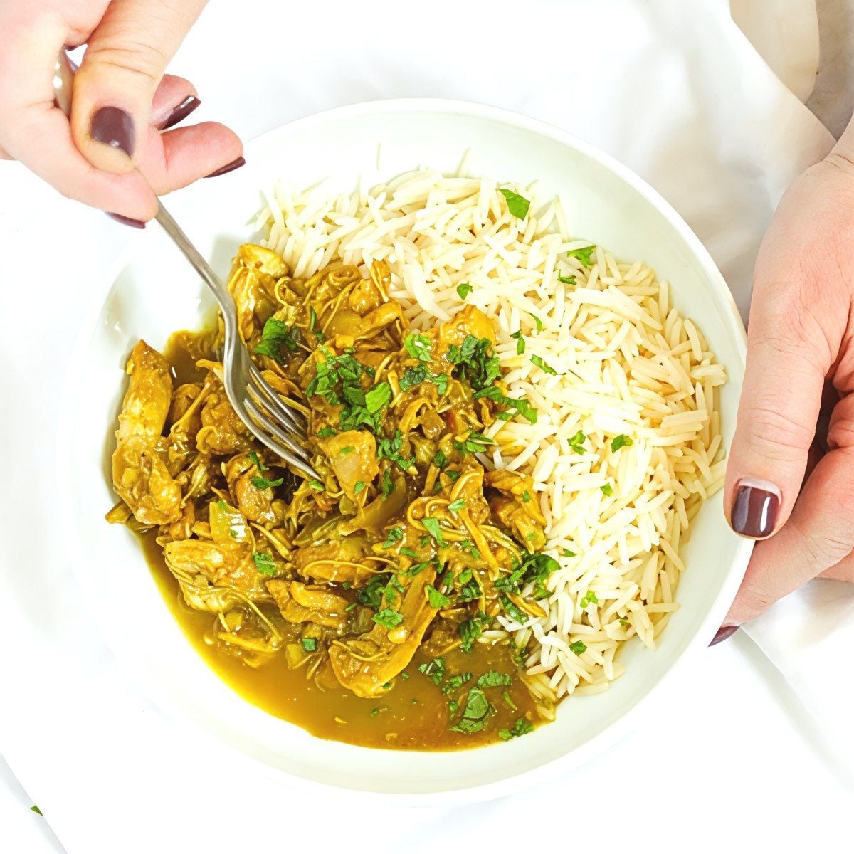A hands-held white bowl of tender slow cooker chicken curry served over basmati rice, perfect for easy dump and go Crockpot chicken dinners.