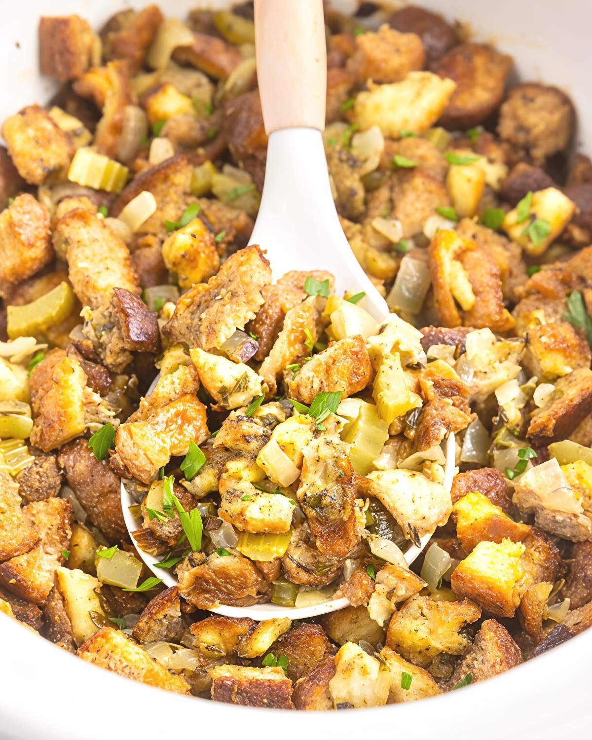 Golden-brown crockpot stuffing thanksgiving recipe with celery, onions, and herbs being scooped directly from a slow cooker.