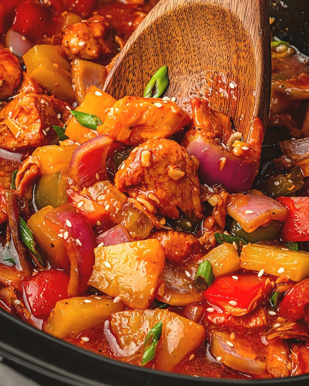A wooden spoon scoops up chunks of sweet and sour chicken with pineapple and vibrant vegetables, showcasing a delicious dump and go crockpot dinners chicken recipe.