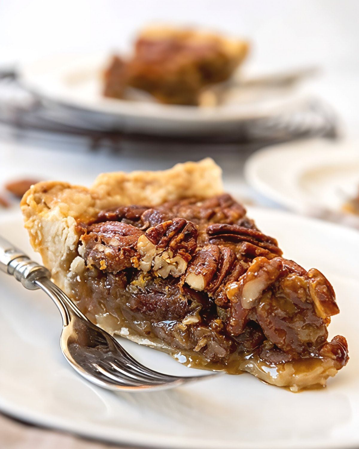 A slice of classic Southern pecan pie featuring a buttery, flaky crust and a rich gooey filling packed with crunchy toasted pecans, served on a white dessert plate with a silver fork