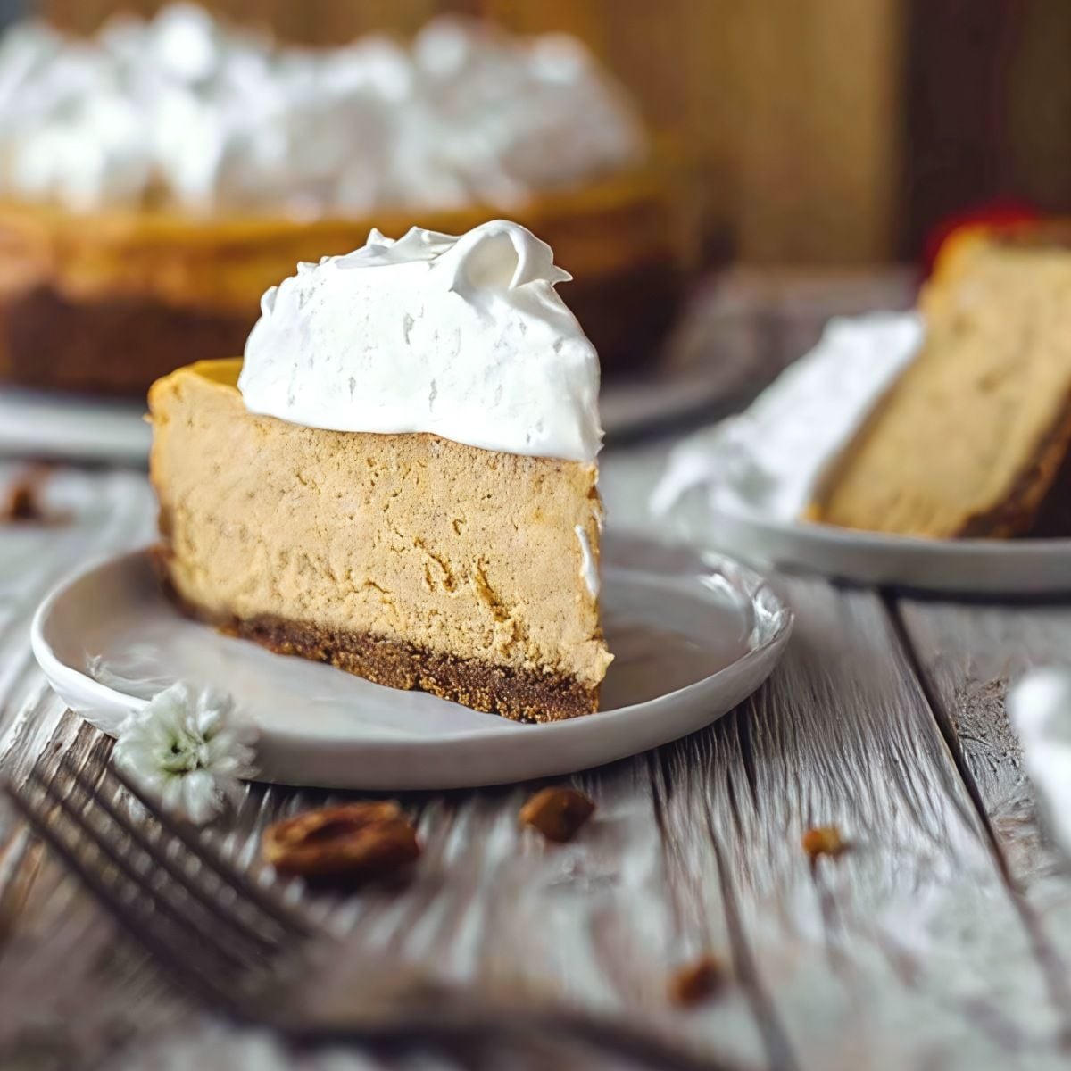 A slice of smooth sweet potato cheesecake on a graham cracker crust, topped with fluffy white marshmallow meringue and set on a rustic wooden table.