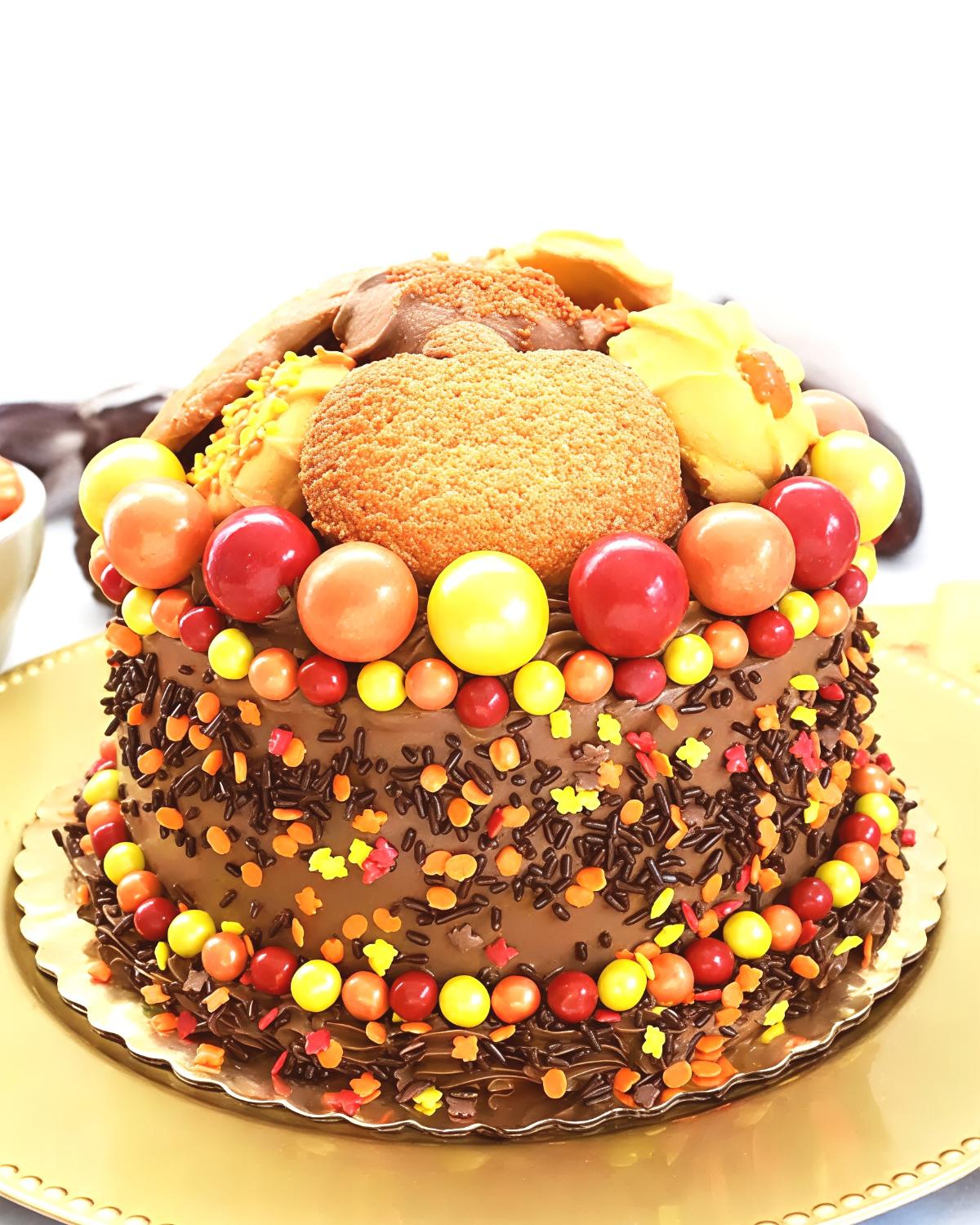 Festive Thanksgiving chocolate cake decorated with fall sprinkles, round candy accents, and pumpkin-shaped cookies on top.