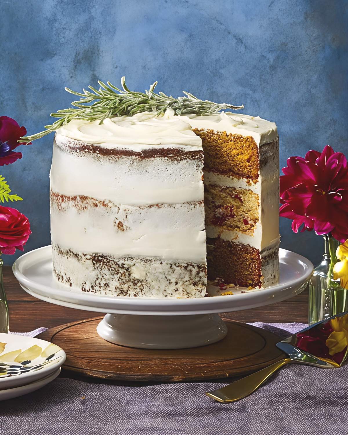 Elegant frosted Thanksgiving layer cake garnished with a sprig of fresh rosemary and vibrant flowers on the sides.