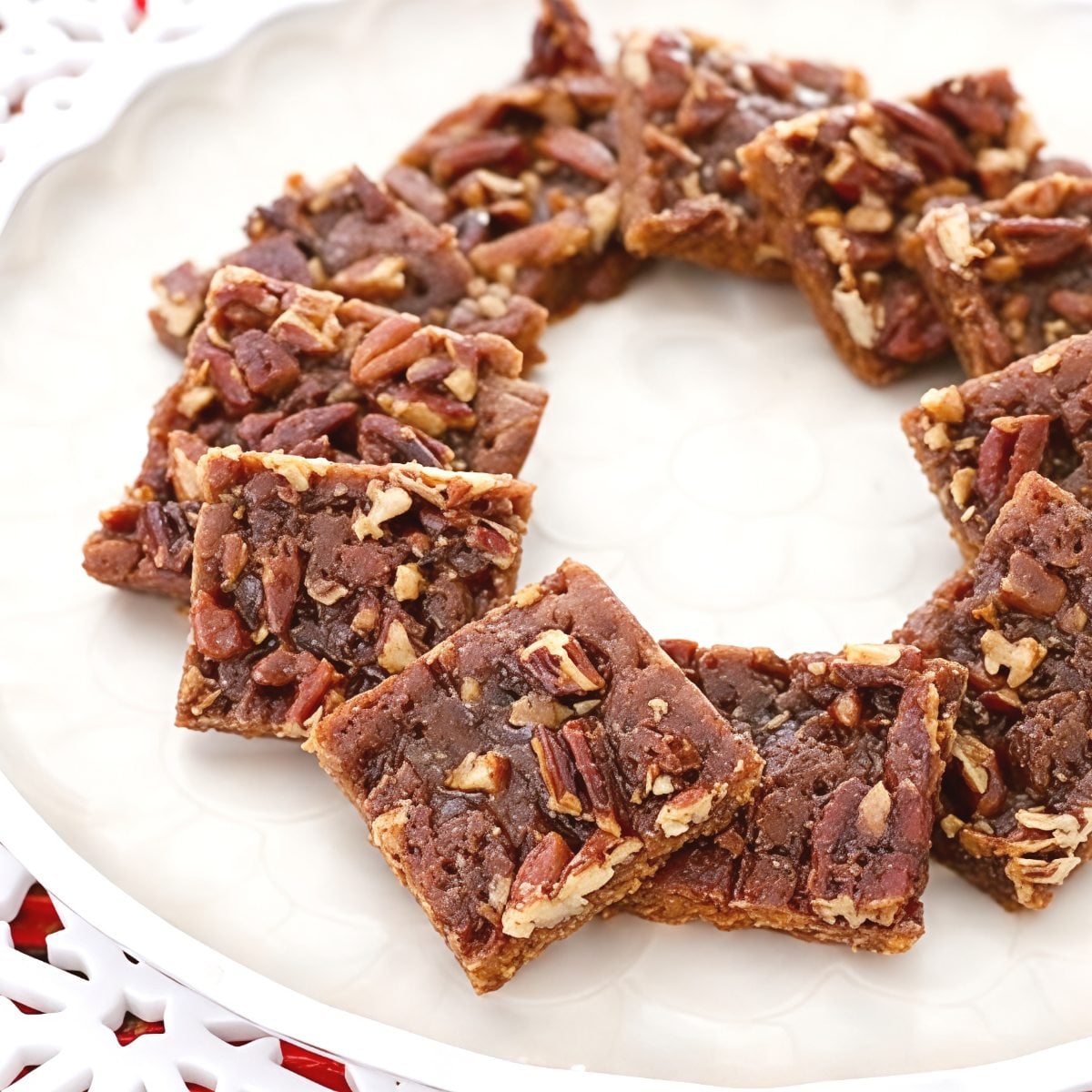 These decadent Thanksgiving cookies feature rich, square pecan praline bars loaded with crunchy toasted pecans and arranged in a ring on a white decorative serving plate.
