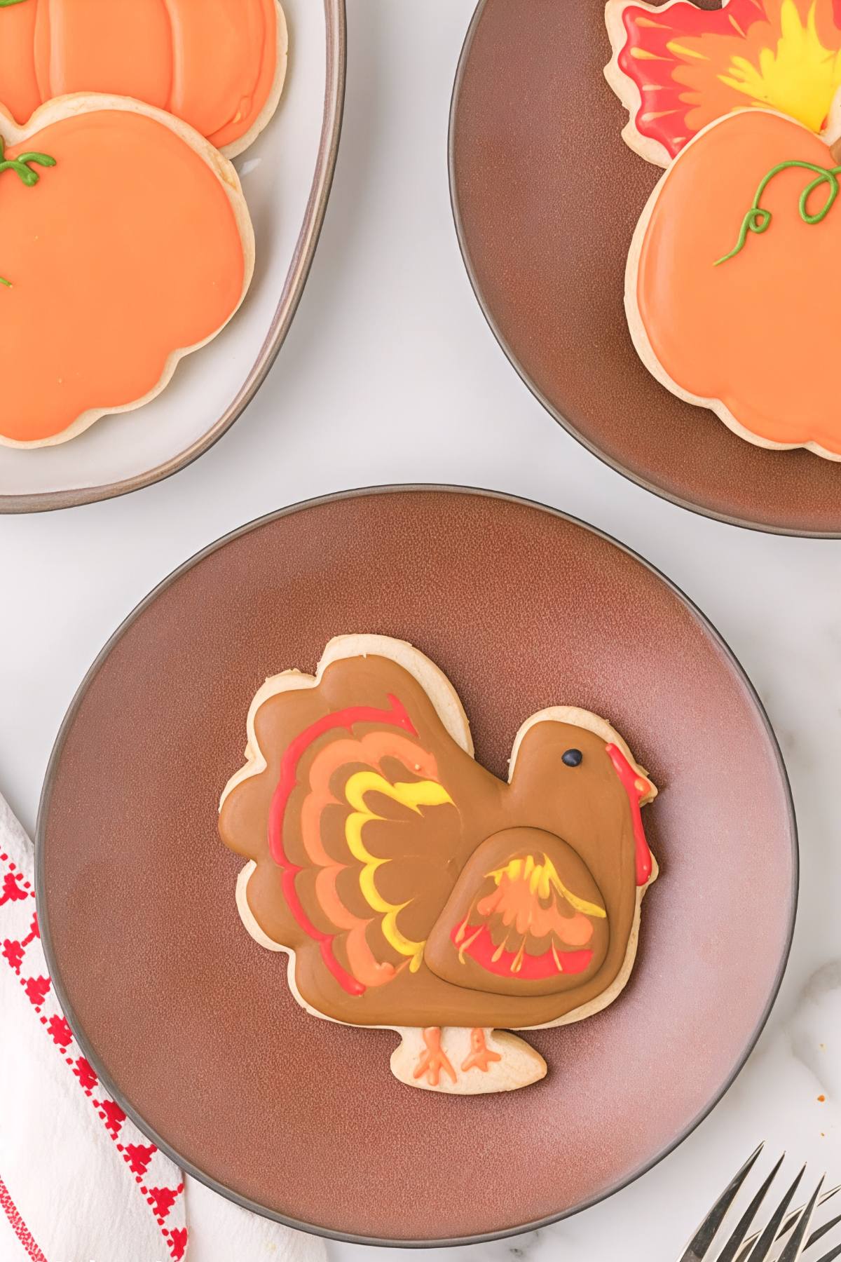 These beautifully decorated Thanksgiving cookies feature a cute turkey sugar cookie centerpiece surrounded by festive pumpkin and autumn leaf designs on plates.
