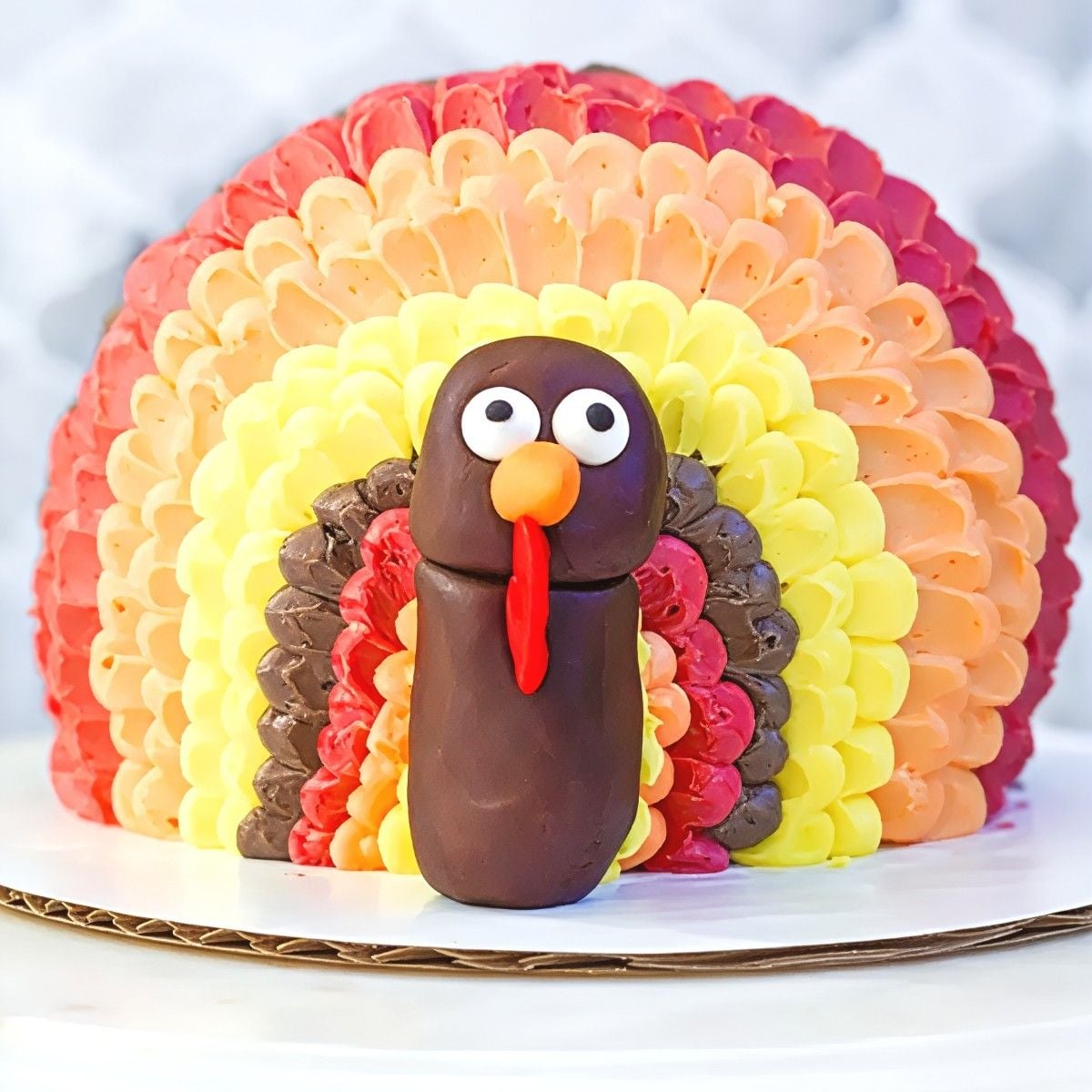 Cute dome-shaped Thanksgiving turkey cake with layered colorful buttercream feather piping and a chocolate fondant turkey head.