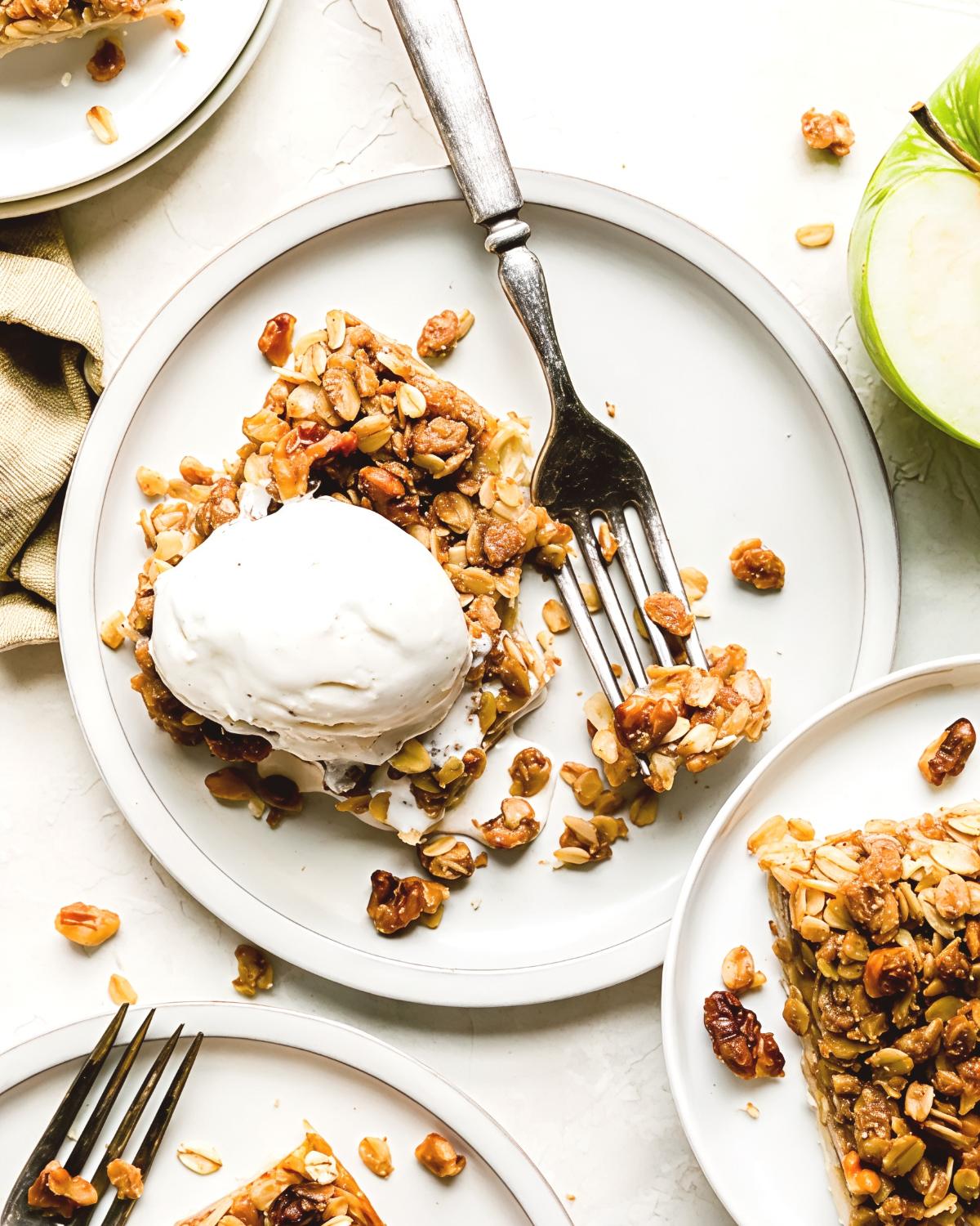 Flaky apple pie bar topped with crunchy walnut oat crumble and vanilla ice cream, served on a white plate as a delicious Thanksgiving dessert idea.