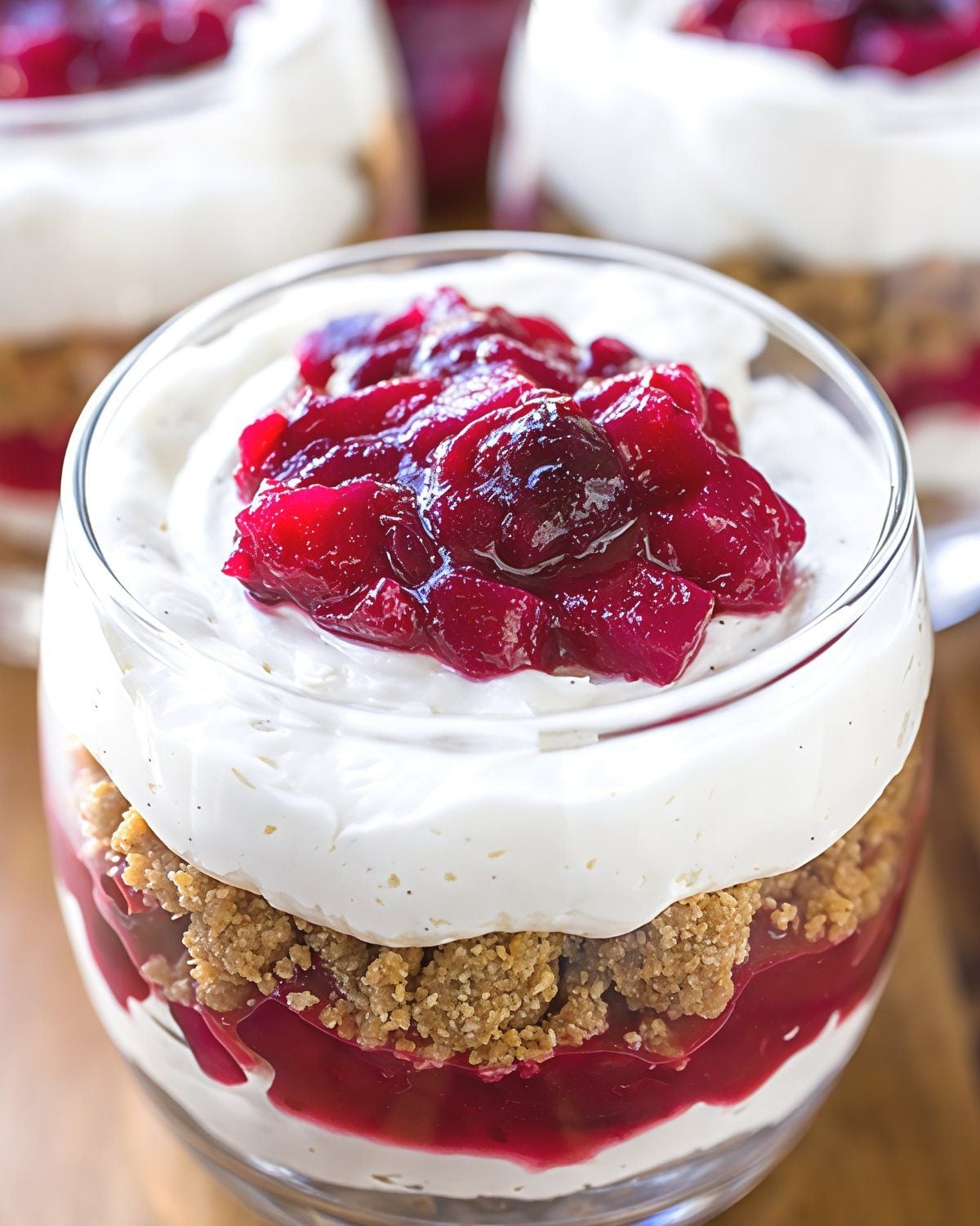 Layered cranberry cheesecake parfait in a glass filled with graham cracker crumbles, cheesecake filling, and sweet cranberry compote for Thanksgiving dessert ideas.