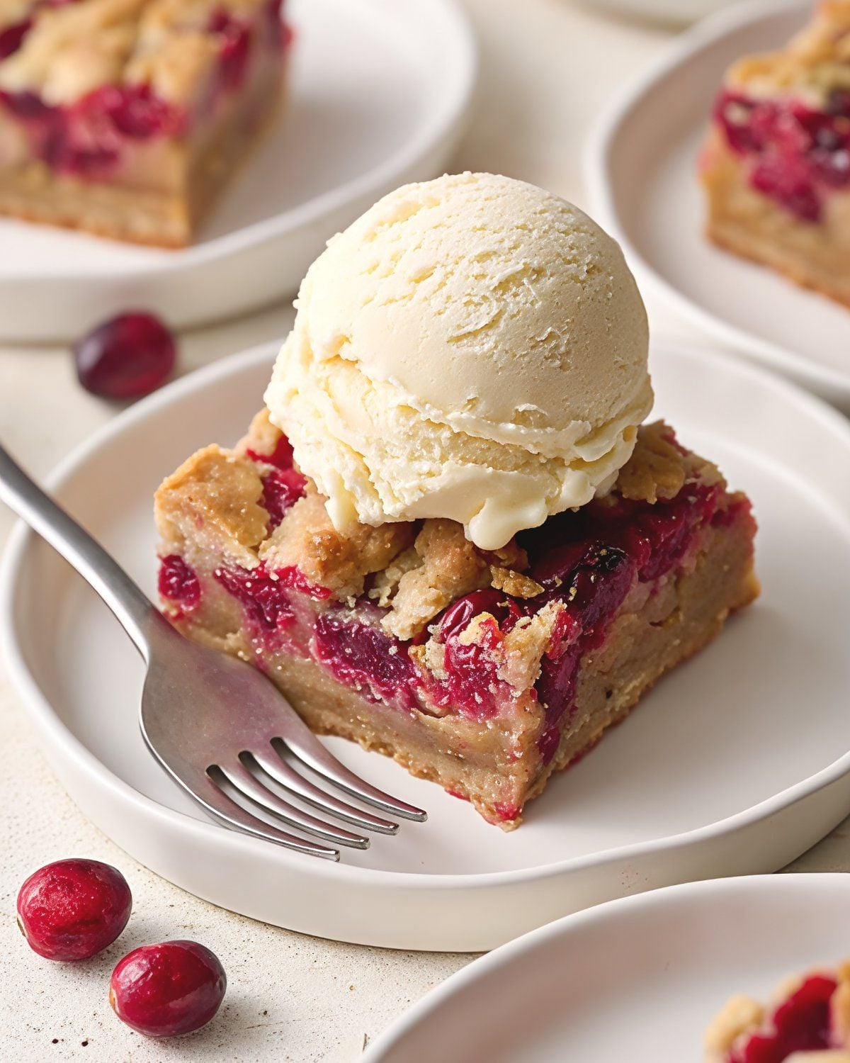Square cranberry crumb bar served on a white plate topped with a scoop of vanilla ice cream, perfect for Thanksgiving dessert ideas.