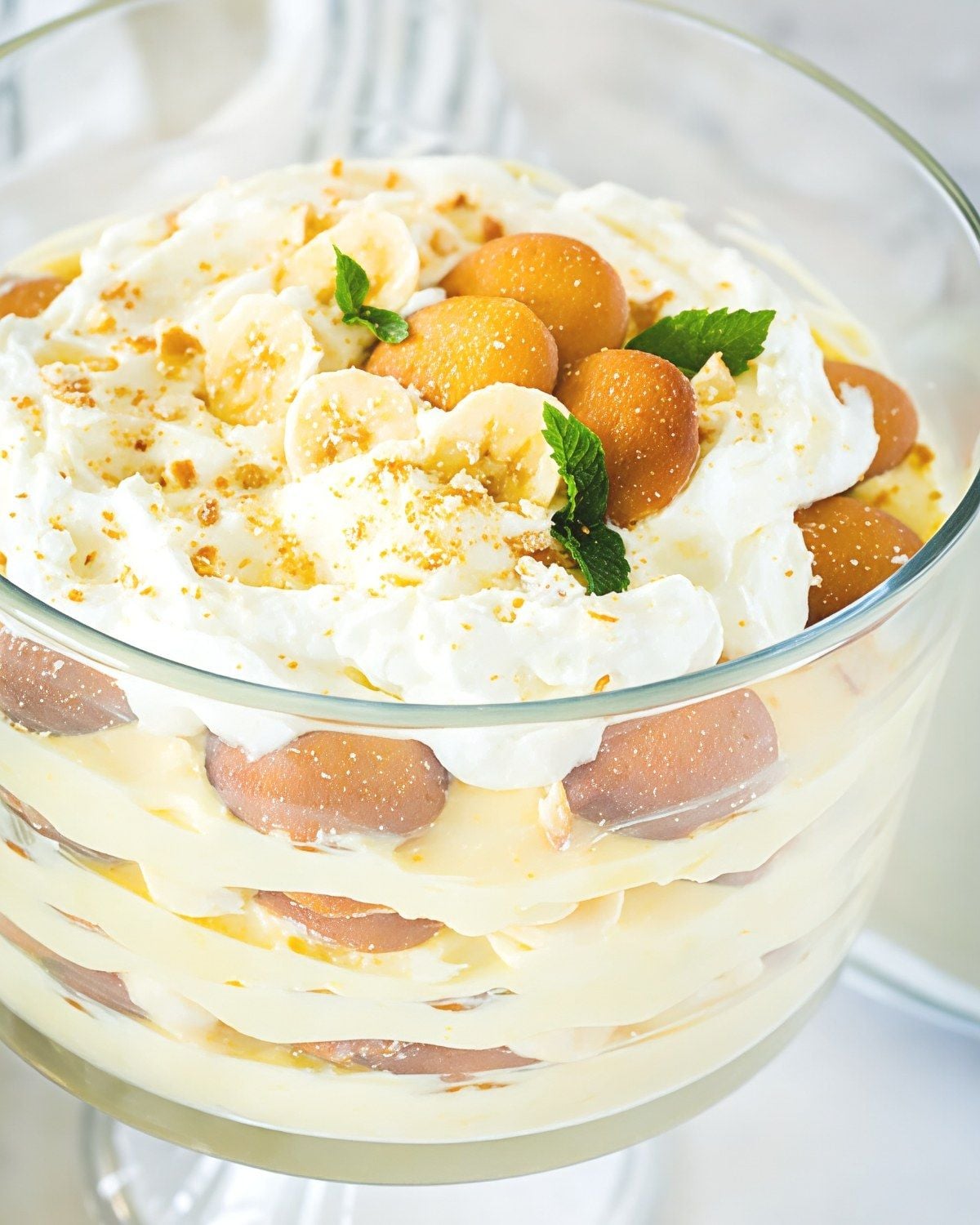 Layered easy banana pudding in a glass trifle dish with vanilla wafers, whipped cream, and sliced bananas, ideal for Thanksgiving dessert ideas.