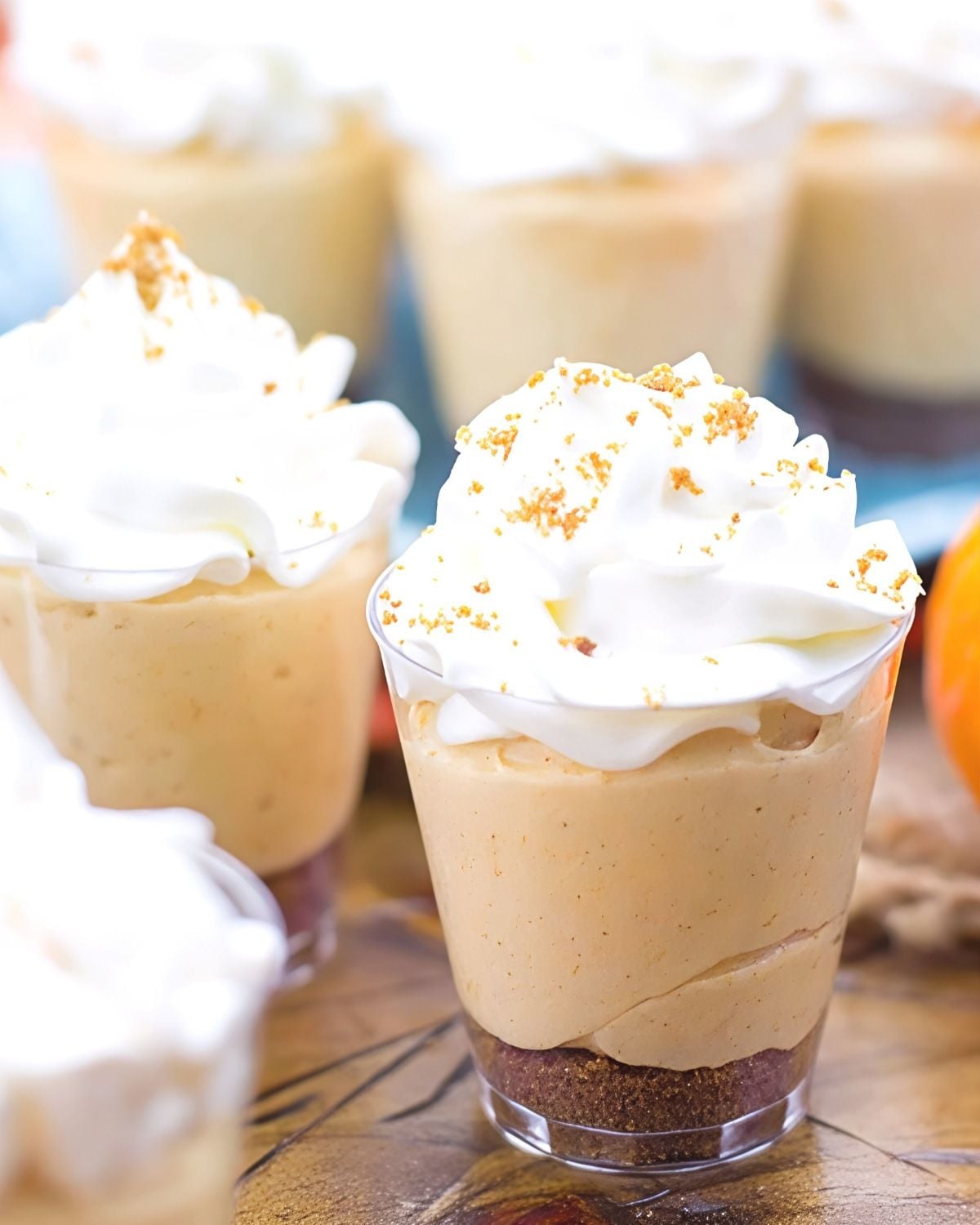 Individual no-bake mini pumpkin pie cheesecake shooters topped with whipped cream and graham cracker crumbs, perfect for easy Thanksgiving dessert ideas.