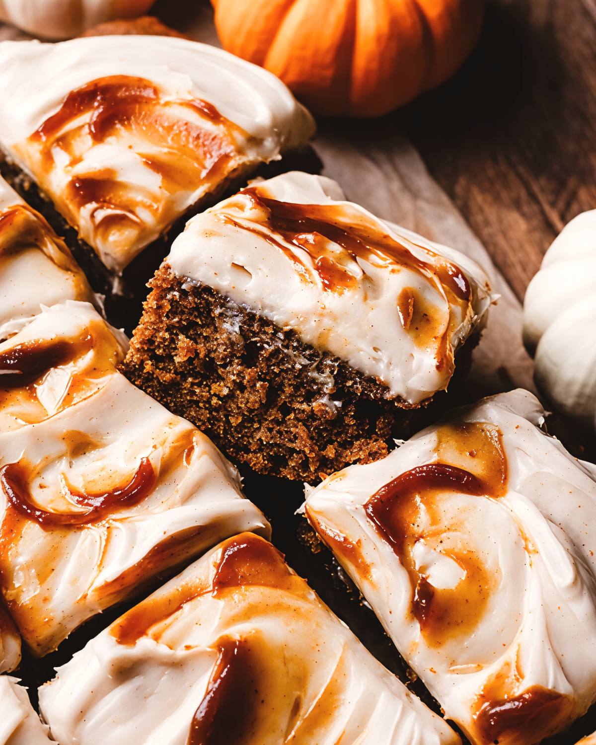 Moist spiced pumpkin bars topped with creamy cream cheese frosting and caramel swirls, perfect for Thanksgiving dessert ideas.