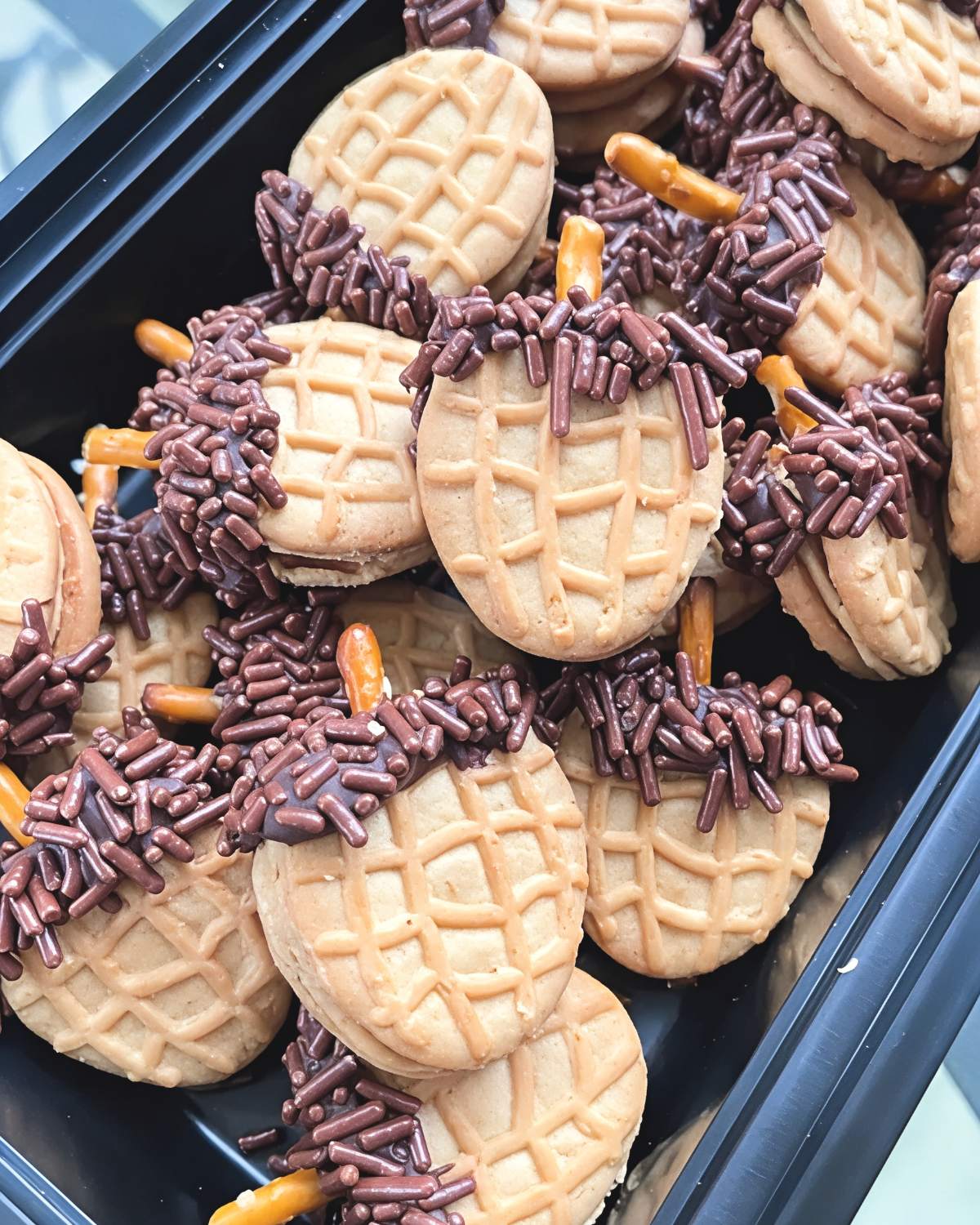 No-bake Nutter Butter acorn cookies dipped in chocolate, coated with chocolate sprinkles, and finished with pretzel stems for cute Thanksgiving dessert ideas.