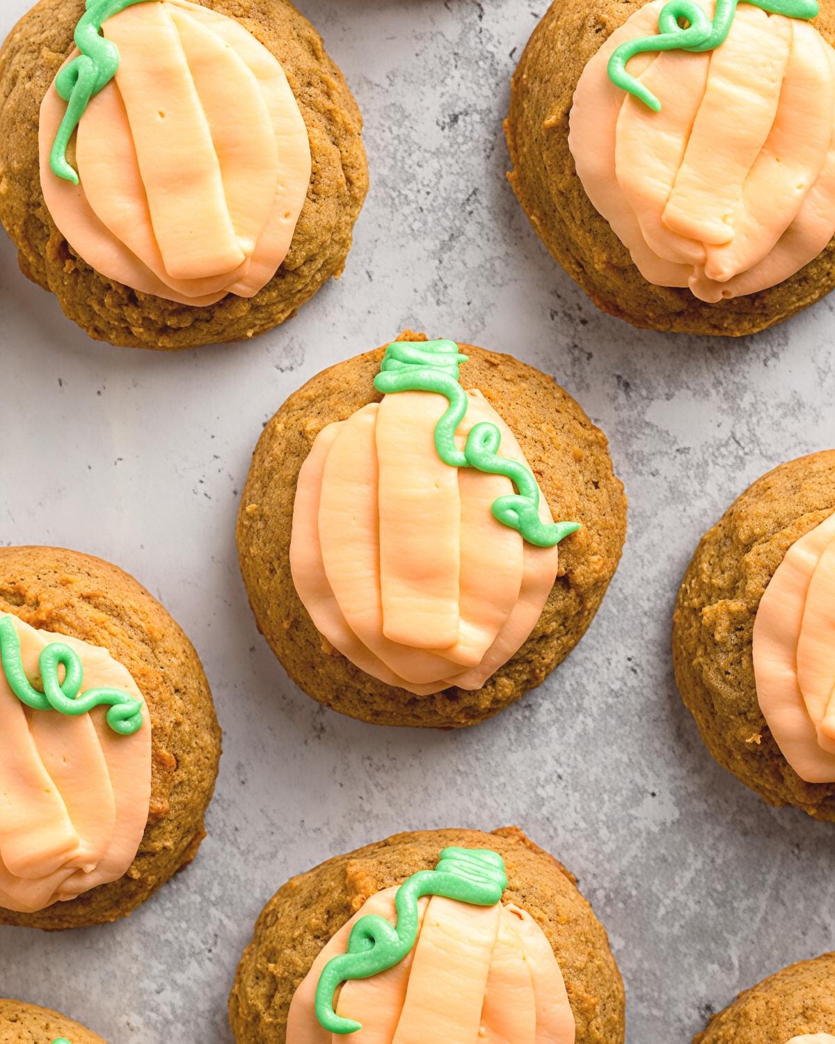 Soft pumpkin cookies topped with orange cream cheese frosting and piped green stems shaped like mini pumpkins, perfect for Thanksgiving dessert ideas.