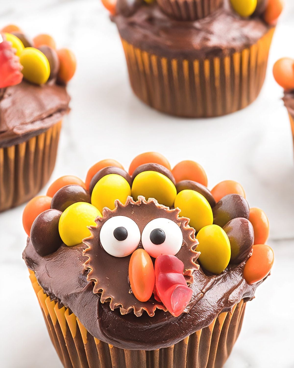 Festive chocolate turkey cupcakes decorated with peanut butter cups, colorful candy feathers, and candy eyes for creative Thanksgiving dessert ideas.