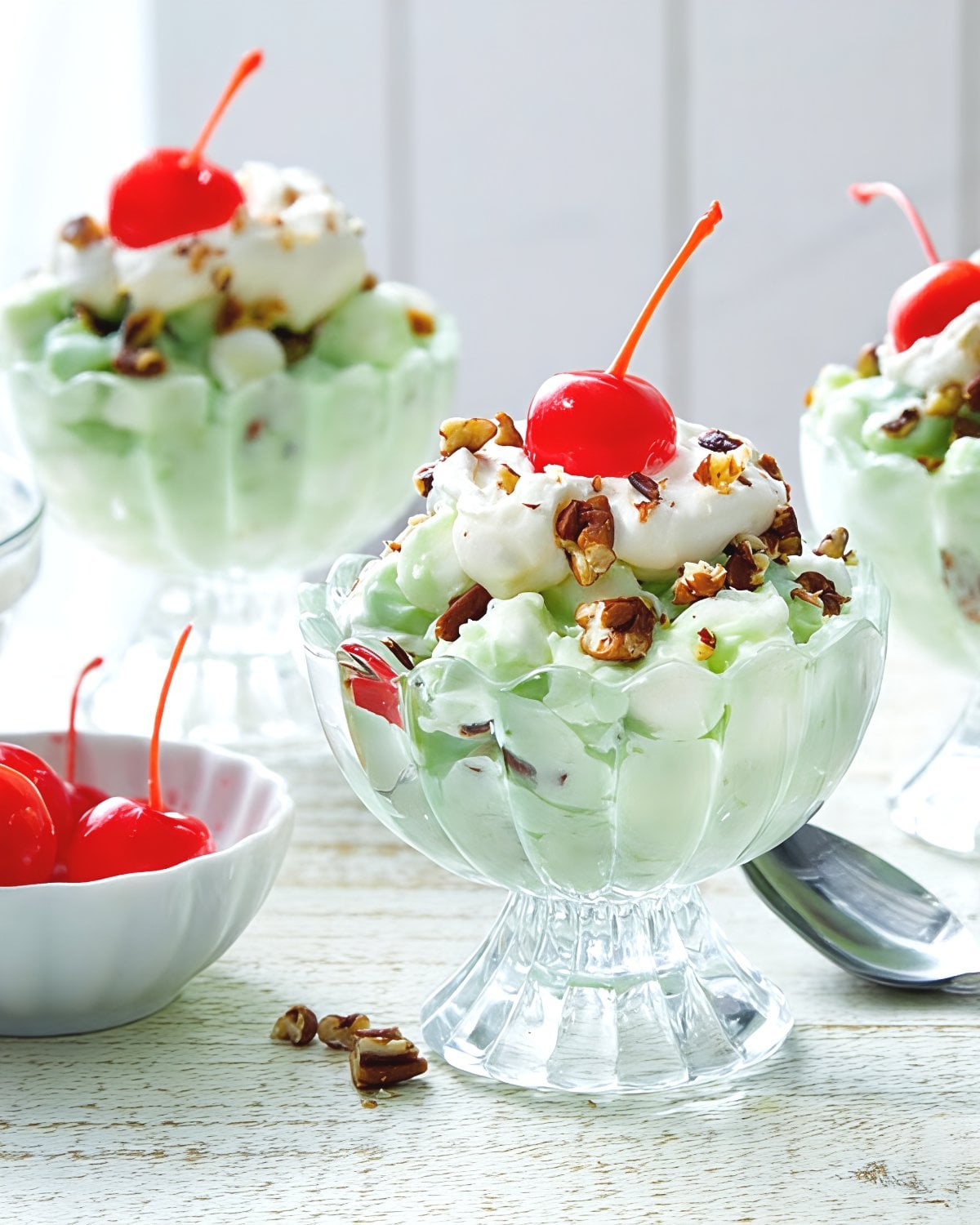 Creamy pistachio Watergate salad served in dessert glasses topped with whipped cream, chopped pecans, and a maraschino cherry for easy Thanksgiving dessert ideas.