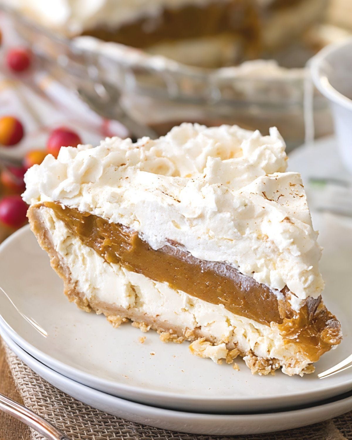 A slice of layered no-bake pumpkin cheesecake with a crust, creamy filling, and a generous topping of whipped cream on a plate for an easy Thanksgiving dessert.