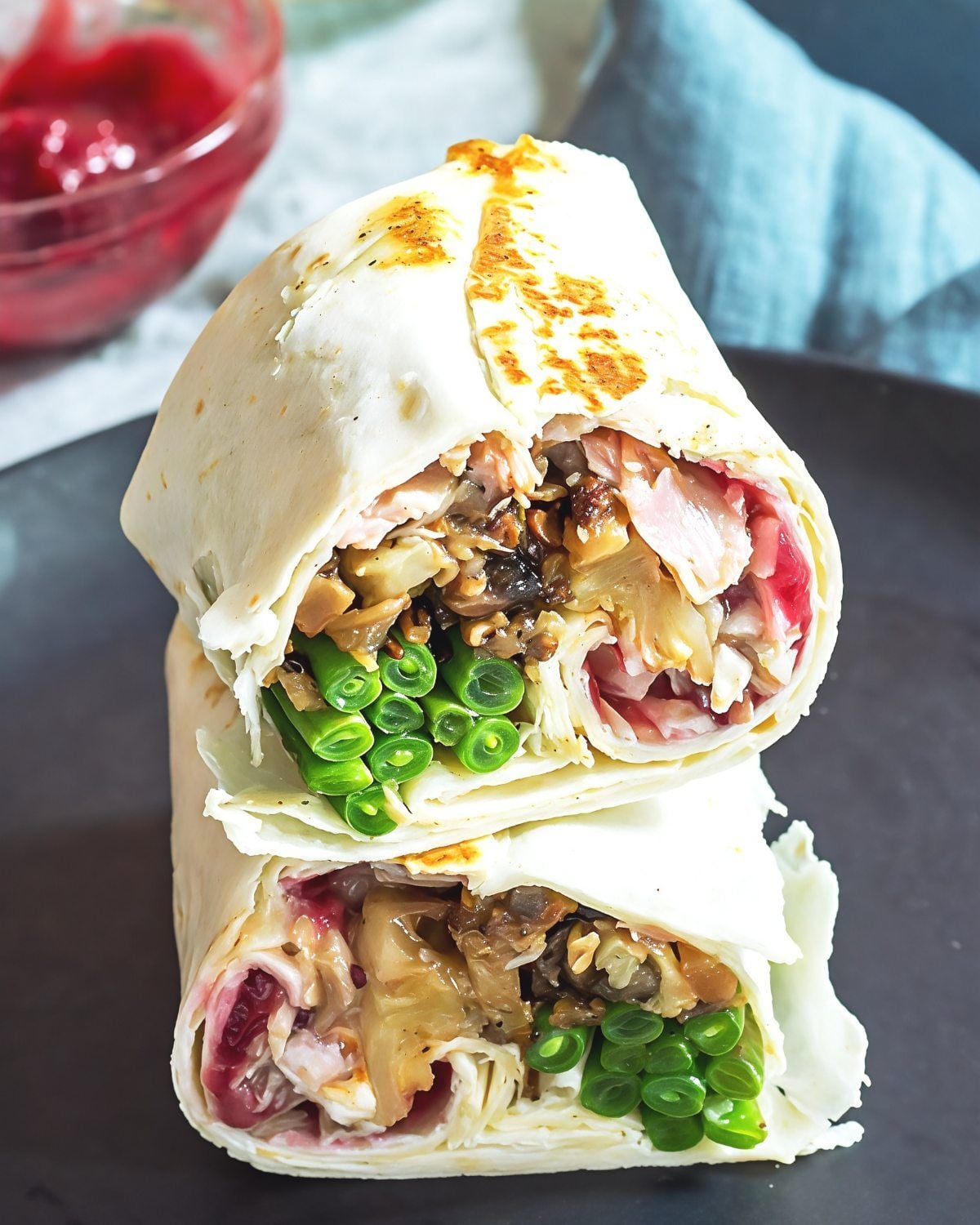 A Thanksgiving leftover burrito sliced in half and stacked to reveal layers of green beans, turkey, stuffing, and cranberry sauce inside a soft flour tortilla.