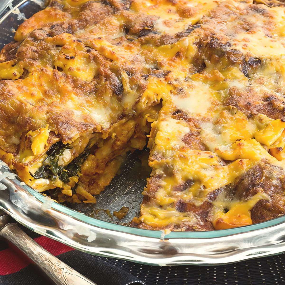 A baked Thanksgiving leftover enchilada pie with melted cheese on top sliced open in a round glass dish to show layered fillings of turkey and greens