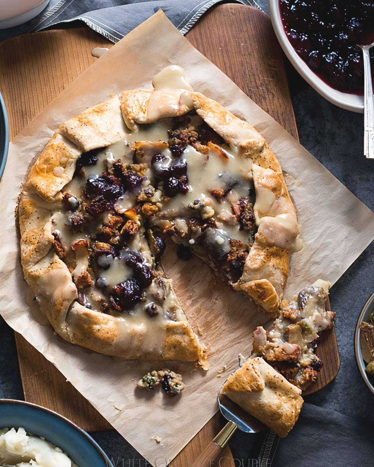 A rustic Thanksgiving leftover galette with a golden pastry crust filled with turkey, stuffing, cranberry sauce, and gravy being served on a parchment-lined wooden board