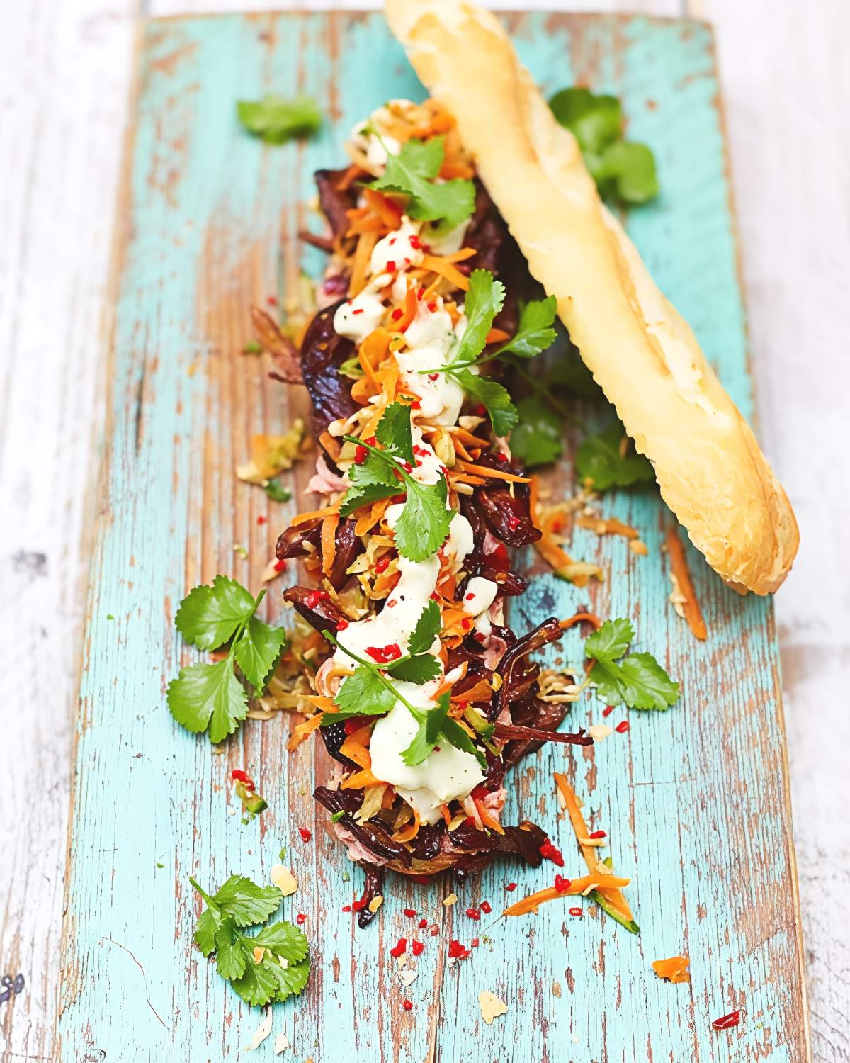 An open-faced Thanksgiving leftover turkey banh mi sandwich served on a rustic wooden board, topped with pickled carrots, creamy mayo, and fresh cilantro leaves.