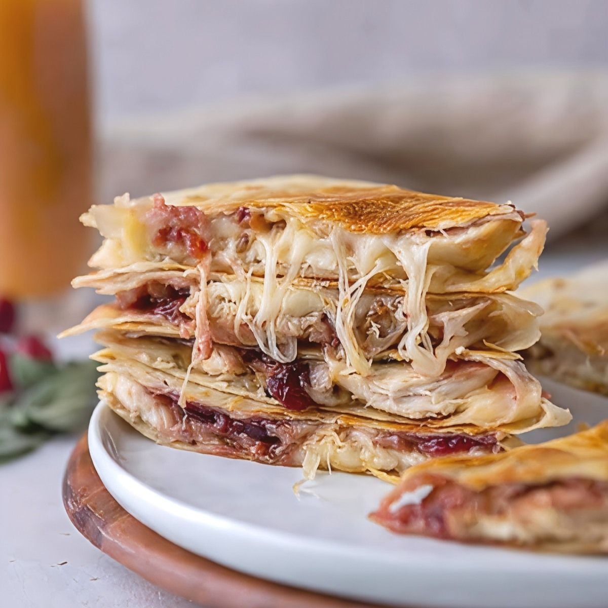 A stack of crispy Thanksgiving leftover turkey quesadillas layered with melted cheese and cranberry sauce served on a white plate.