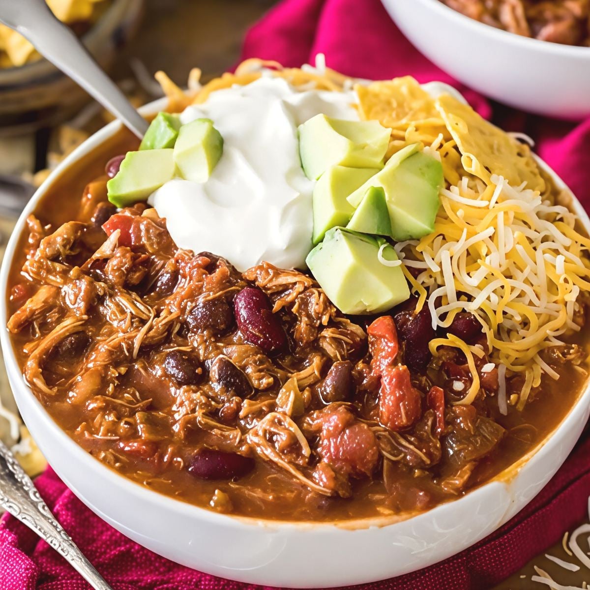 Hearty leftover turkey chili packed with kidney beans and tomatoes, topped with sour cream, diced avocado, and shredded cheddar cheese in a bowl.
