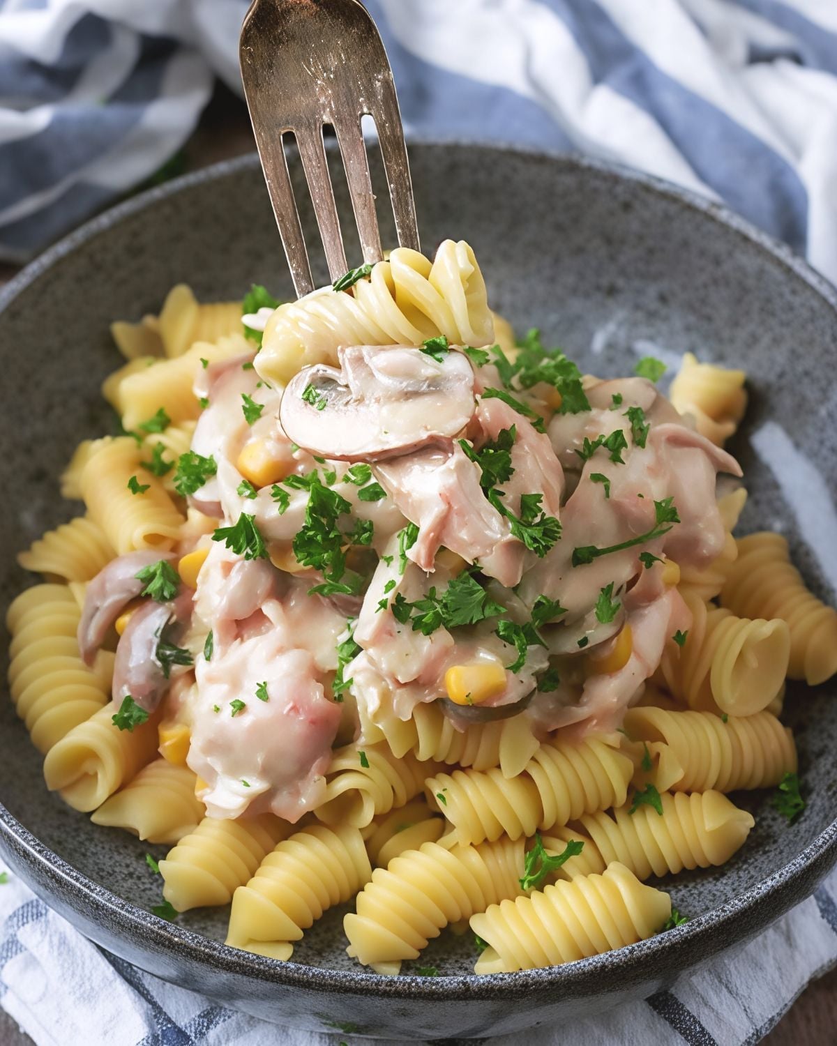 Creamy turkey fricassee with mushrooms, corn, and fresh parsley served over rotini pasta in a bowl.