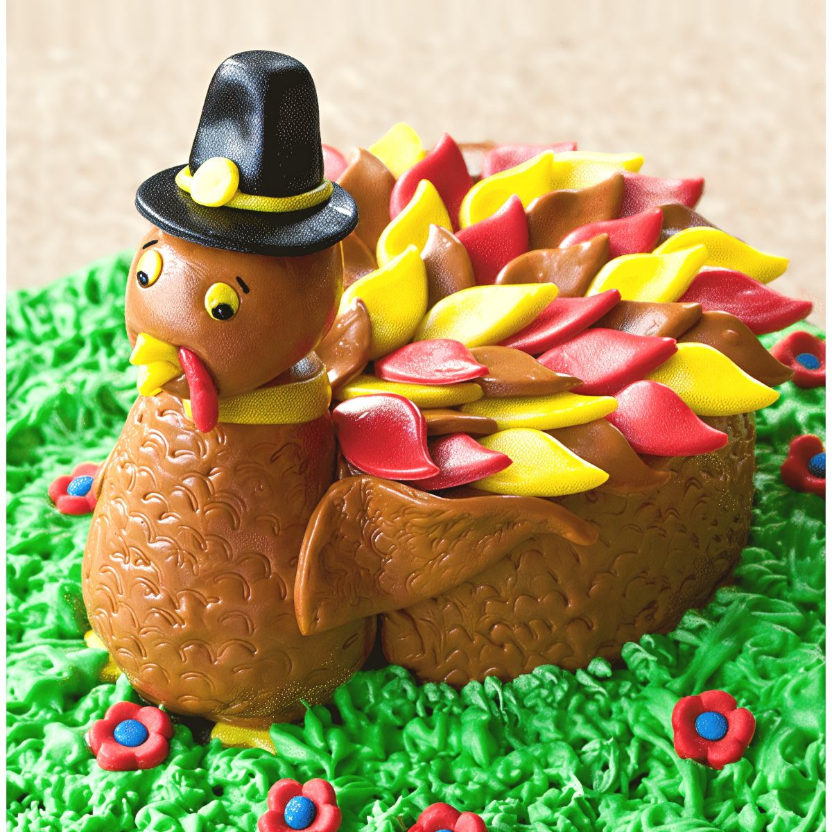 Cute Thanksgiving turkey cake shaped like a turkey with a black hat, colorful feather decorations, and green frosting grass base.